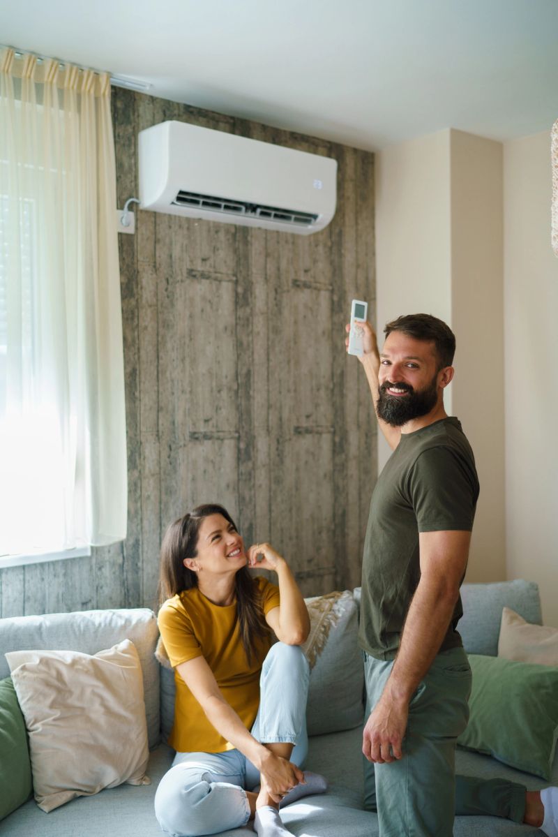 Young couple relaxing in living room, man operating air conditioner with remote.