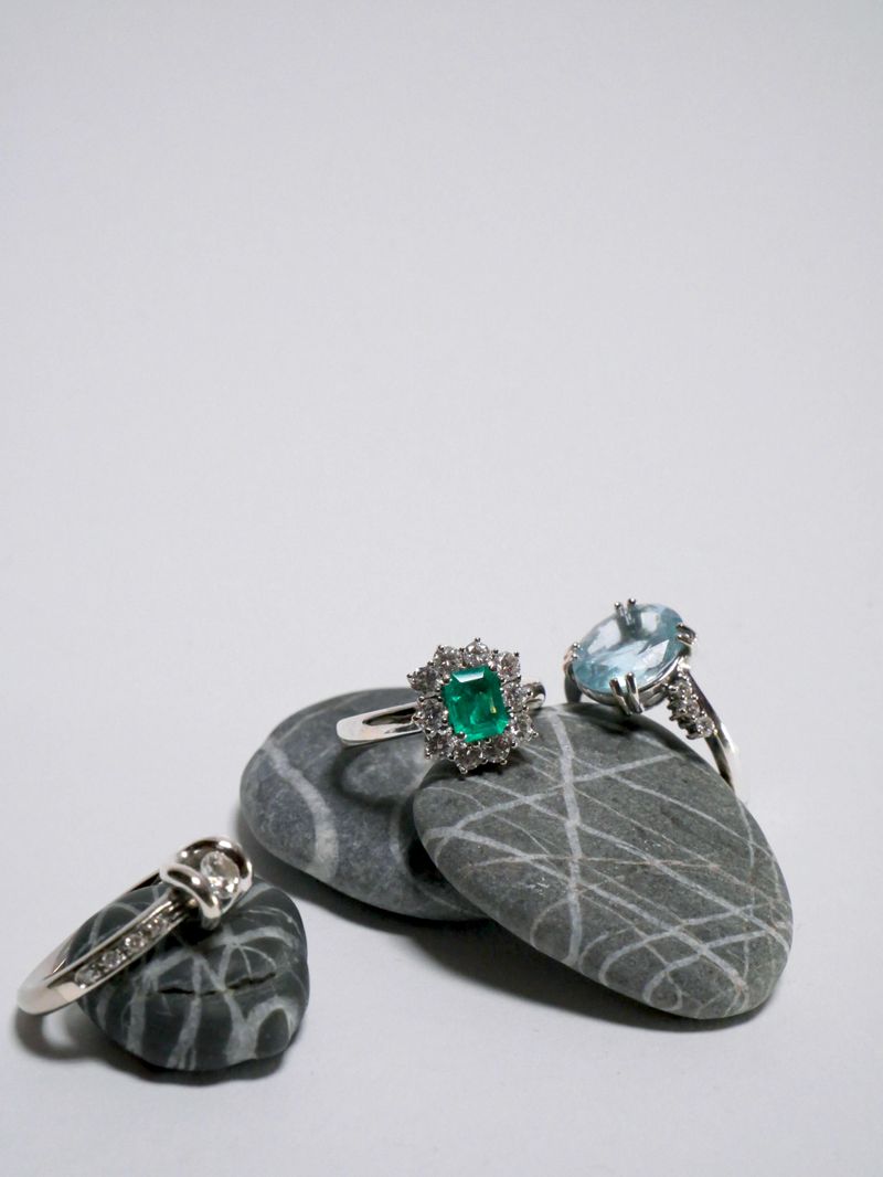 three rings (diamond, emerald and aquamarine) on some pebble stones on a white background