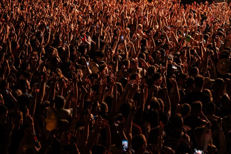 Fans raising hands and capturing videos with smartphones during an exhilarating live music concert, surrounded by vibrant lights and energy