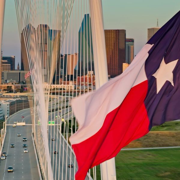 Bandera de Texas ondeando frente a un puente y la ciudad.