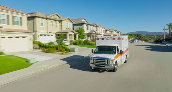 An ambulance driving through a suburban neighborhood on a clear day.