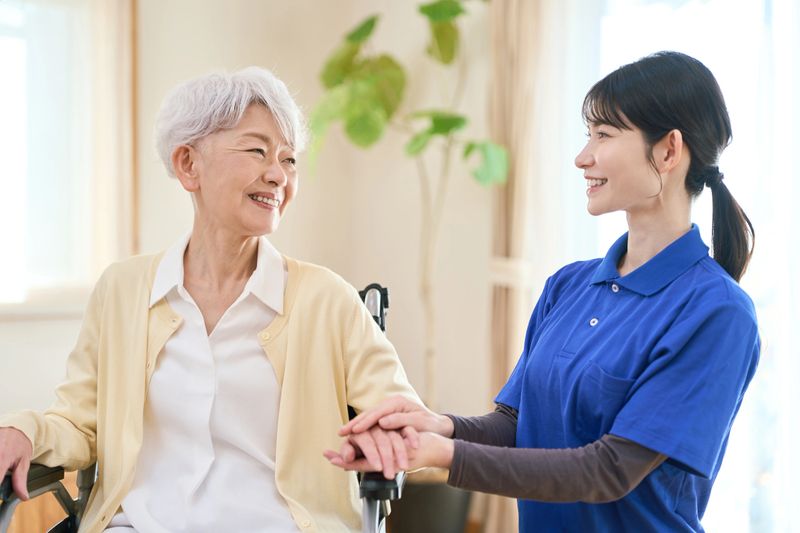 Asian visiting caregiver holding a senior's hand