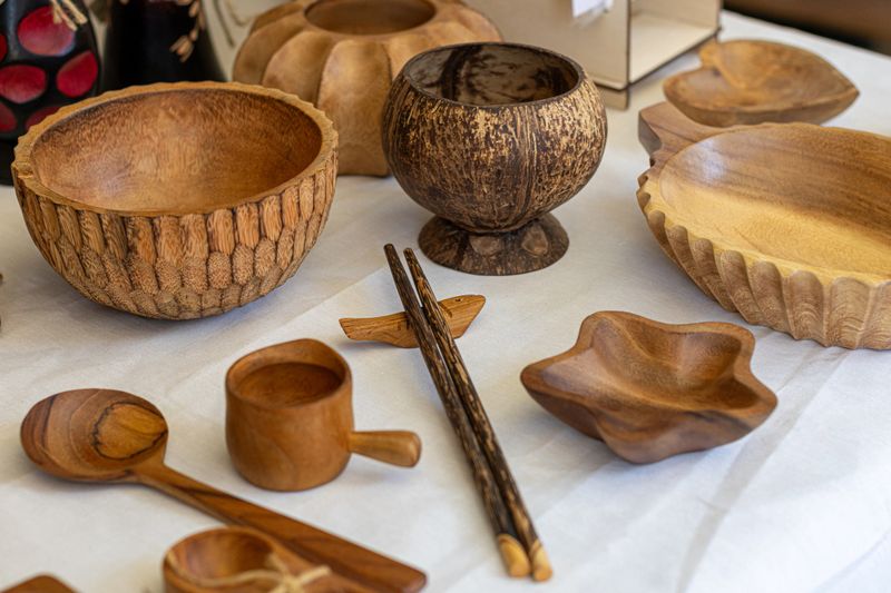 A beautiful assortment of handcrafted wooden bowls, spoons, cups, and chopsticks displayed on a white table, showcasing natural textures and unique designs perfect for rustic home decor or sustainable kitchenware.