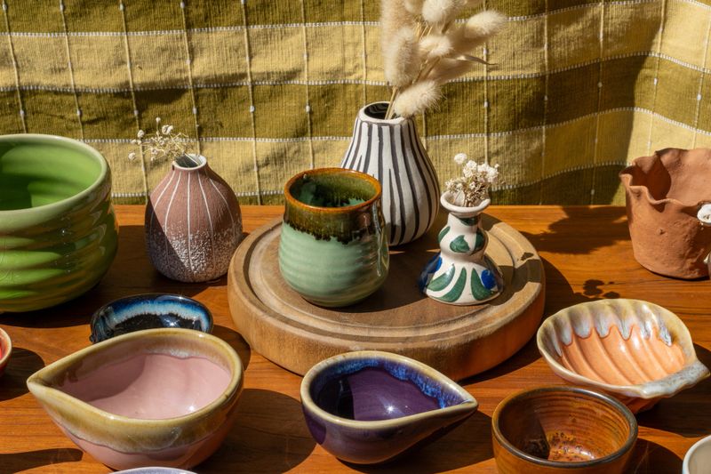 This vibrant array of unique hand-crafted ceramic pieces, featuring bowls, cups, and vases with various glazes, is perfect for home decor and everyday use.