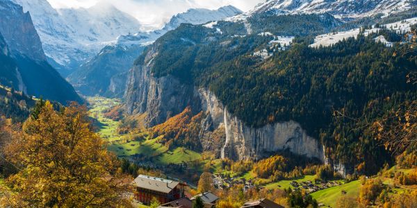 Scenic valley with autumn trees and snow-capped mountains in the background.