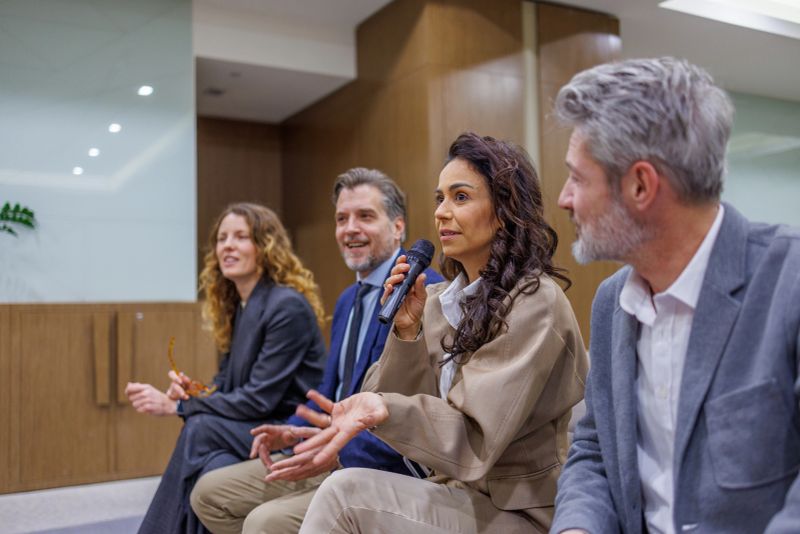 Group of business people engaging in a seminar, one woman holding a microphone and gesturing while presenting to an audience