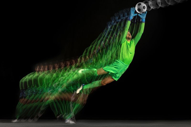 Goalkeeper catching ball in mid air stroboscope sequence on dark background. Concept of precision timing, athletic control, sports advertising and performance study.