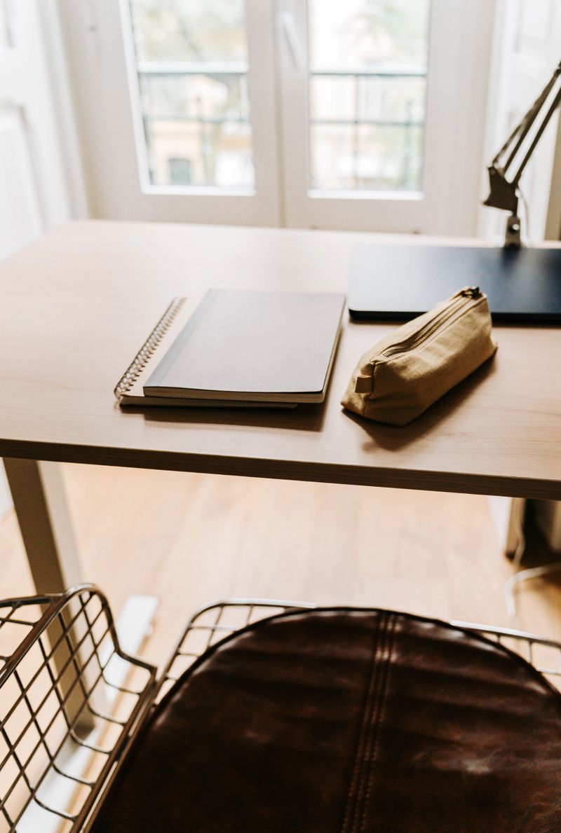 Minimal workspace with notebook and pencil case on a wooden desk near a bright window, with soft natural daylight in a modern interior