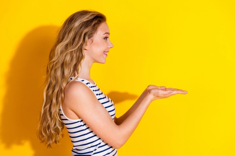 A charming young woman in casual summer attire poses against a vibrant yellow background, creating a bright and dynamic scene, showcasing happiness and a presenting gesture.