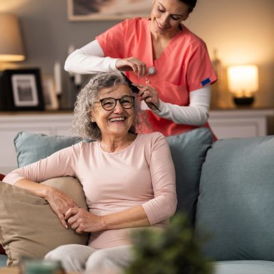 Nurse examining elderly woman's ear at home.