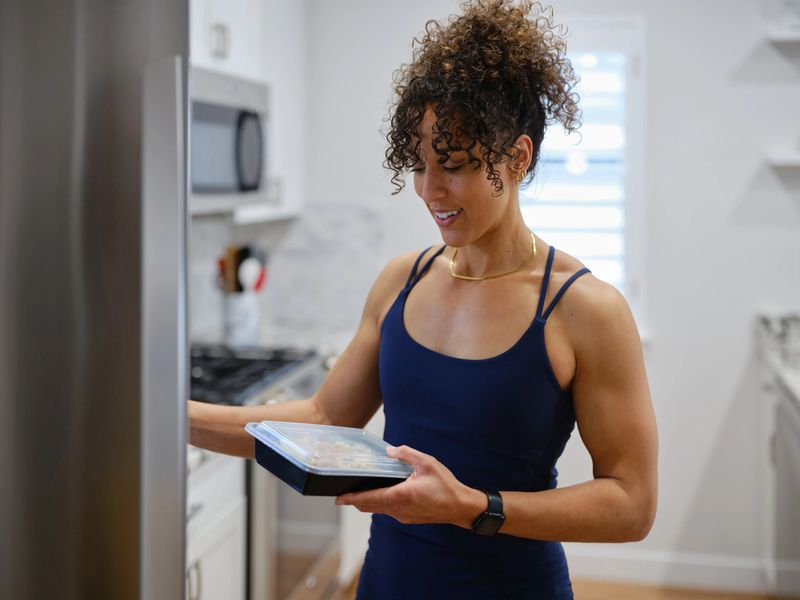 A fit young woman in a home preparing and eating a prepared meal.