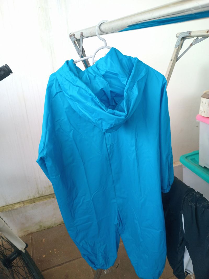 Blue hooded raincoat or waterproof jacket hanging on a drying rack indoors, minimalist laundry scene with clean white background and copy space.