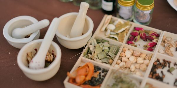 Mortar and pestles with various herbs and spices in a wooden tray.