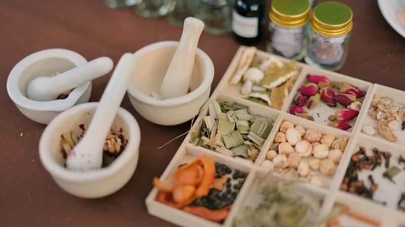 Collection of traditional herbal ingredients arranged beside mortar and pestle used for natural remedy preparation. Assorted dried herbs, spices, and botanical elements representing holistic wellness, alternative medicine, organic lifestyle, and traditional healing practices. Strong concept for healthcare lifestyle, wellness branding, natural therapy promotion, and herbal product marketing.