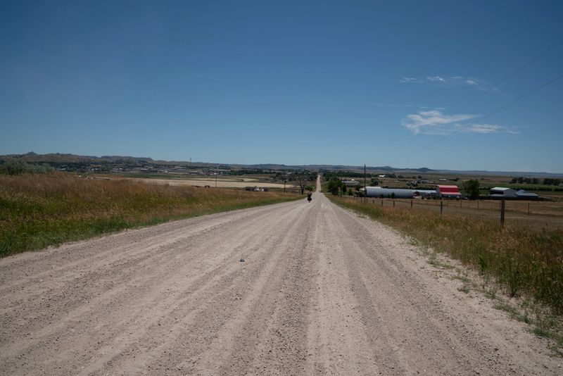 A lone cyclist in protective gear rides a mountain bike on a sunlit gravel path through open fields, evoking adventure and freedom.