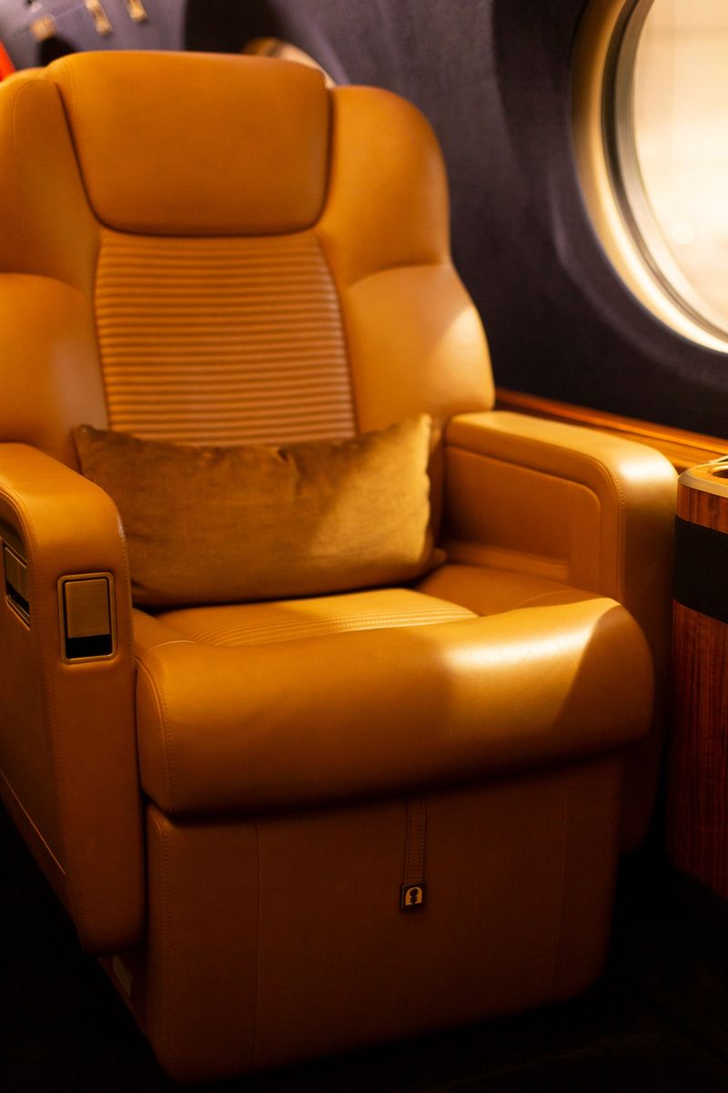 Plush leather seat Gulfstream G cabin with soft pillow and window glow, deep recline function, warm tan tones and ambient lighting creating calm, private atmosphere for rest