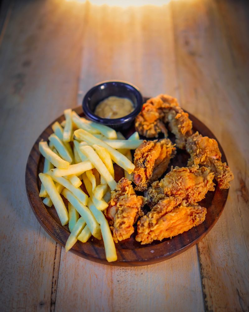 Golden fried chicken wings and french fries served on a wooden board with a side of creamy dipping sauce.