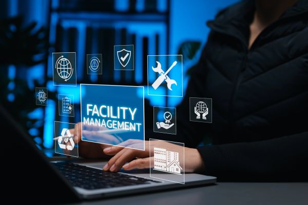 Person working on laptop with facility management icons floating above keyboard.