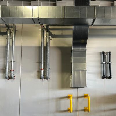 Industrial pipes and vents on a wall with yellow handles.