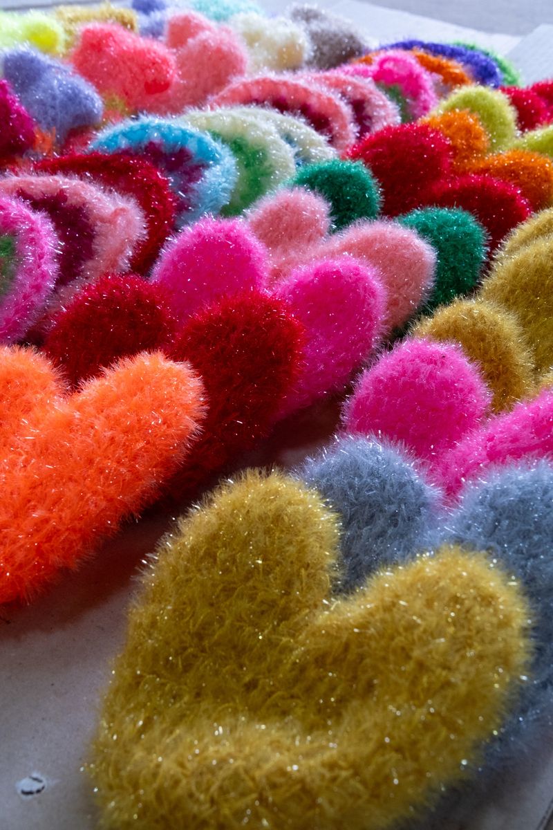 A vibrant, close-up shot of several handmade heart-shaped scrubbers in various colors.