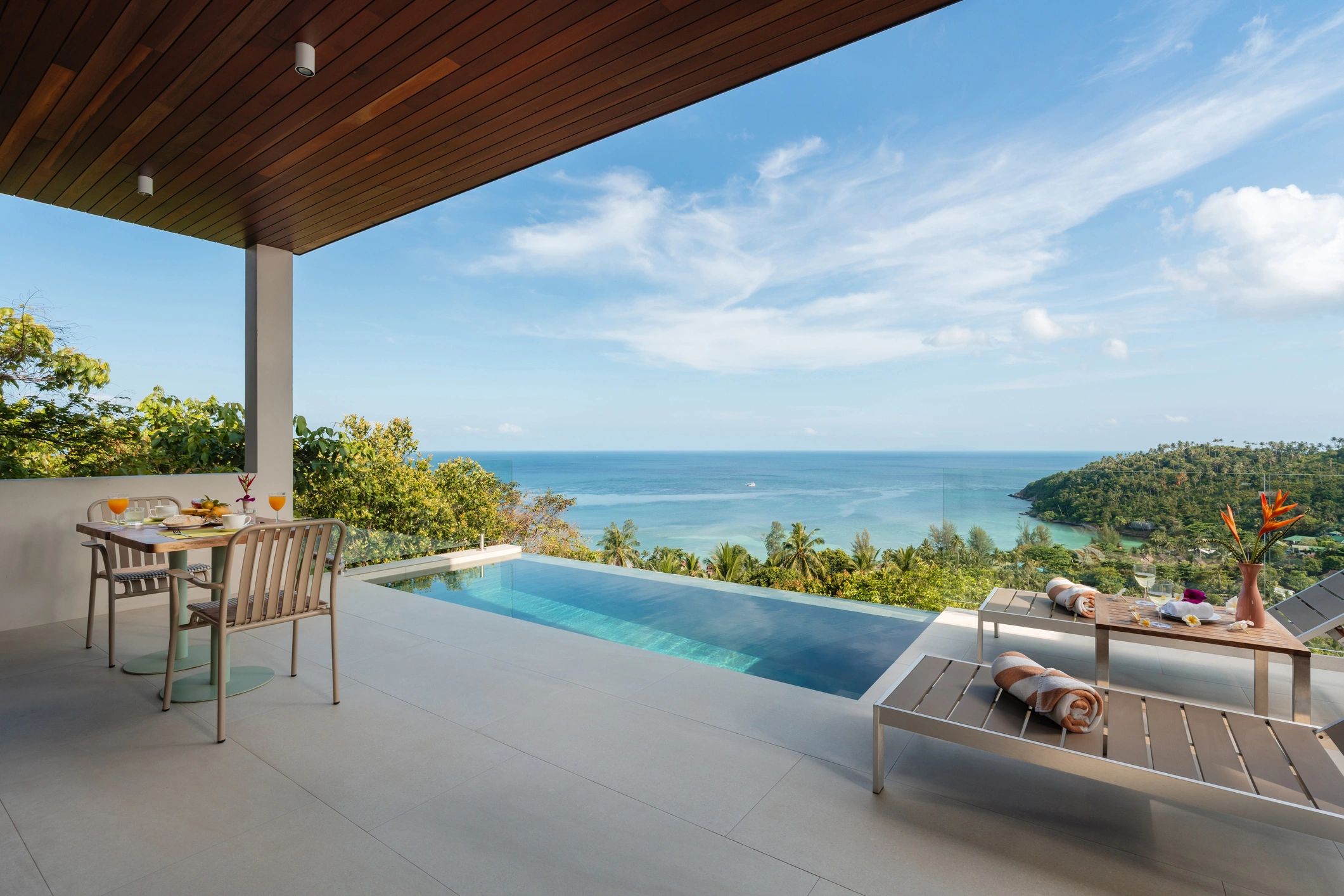 Luxury patio with pool overlooking ocean and tropical greenery.