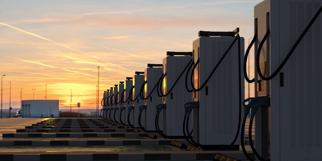 Row of electric vehicle charging stations at sunset.
