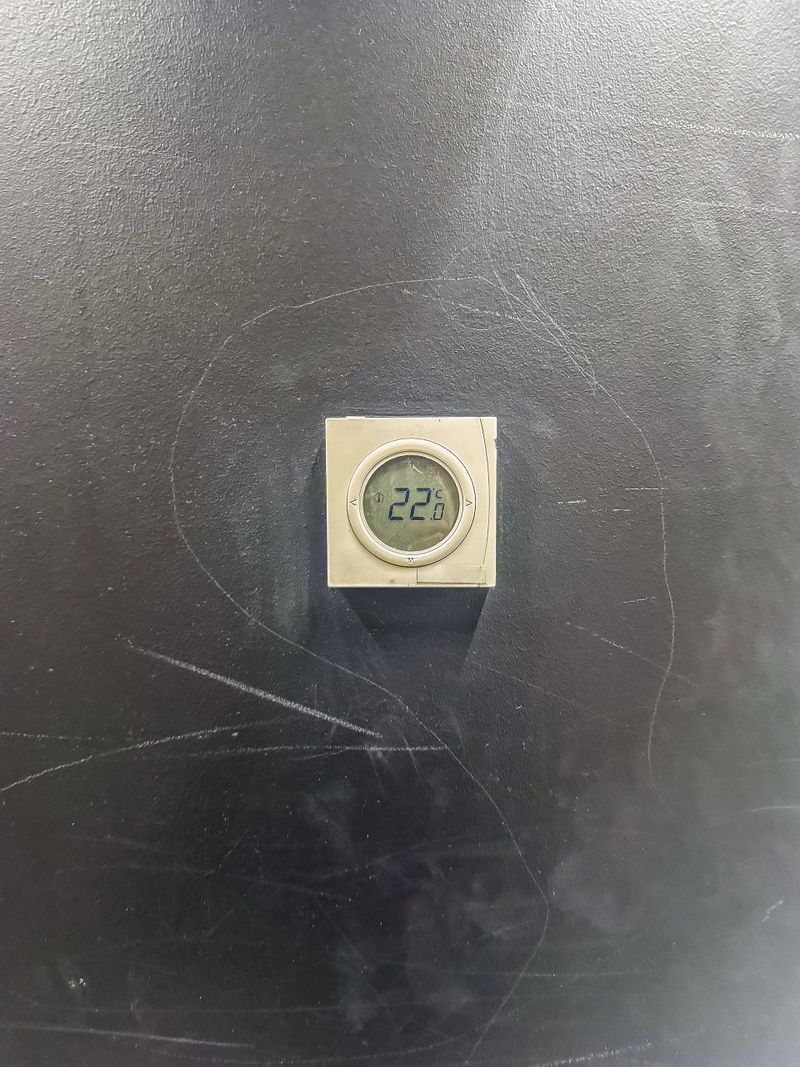 Climate control concept. A minimalist square digital thermostat displays a comfortable temperature on a dark, textured, and worn surface.High quality photo