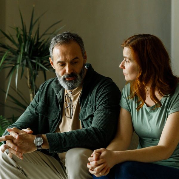 A man and woman sit closely, engaged in a serious conversation indoors.