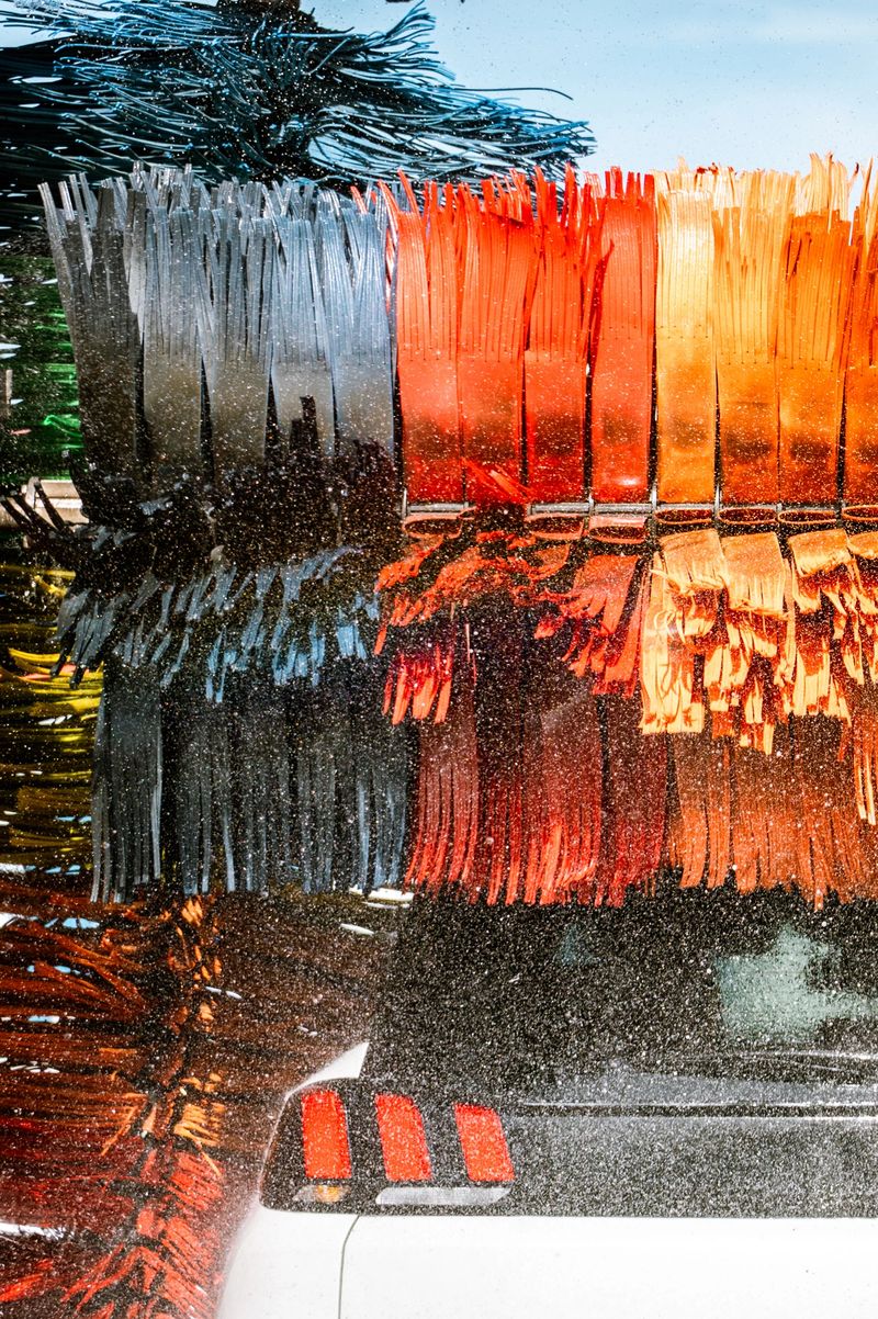 Close-up of rotating wash rollers scrubbing vehicle roof with water and foam.