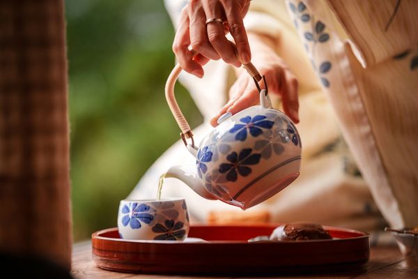 Pouring tea from a floral teapot into a matching cup.