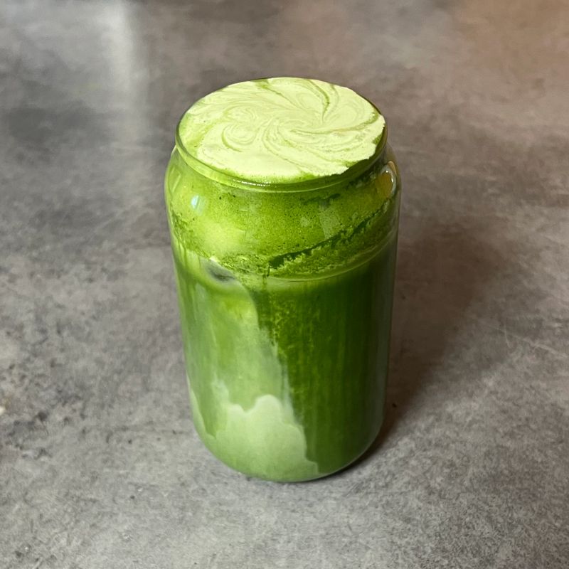 Matcha latte in a clear cup with vibrant green color, topped with creamy froth, highlighting smooth texture, swirling patterns, and refreshing appearance in close-up detail