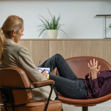 Patient lying on couch talking to therapist taking notes.