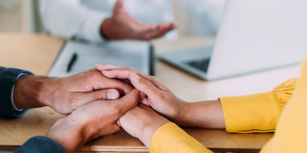 Two people holding hands across a desk in a comforting gesture.