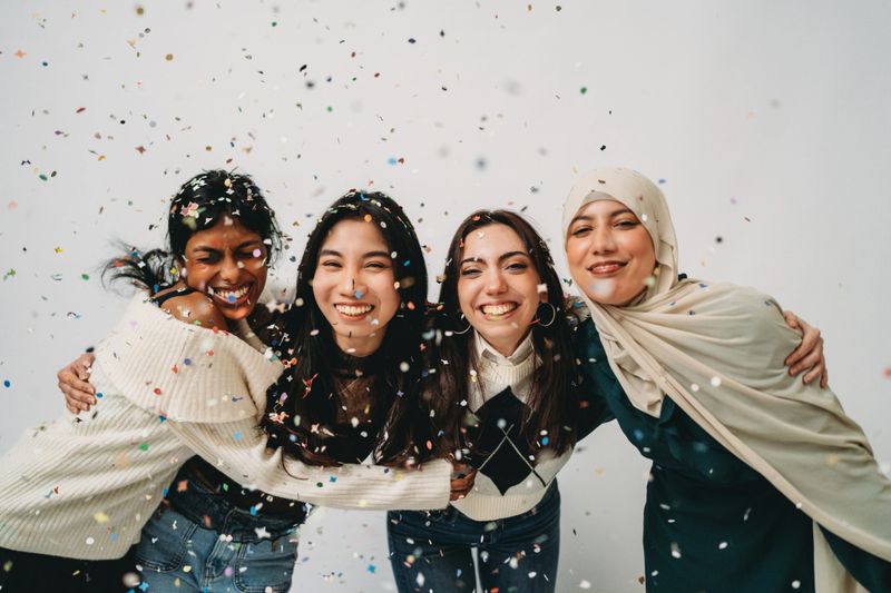 Young diverse women embracing and smiling during a party with confetti, celebrating inclusion and happiness