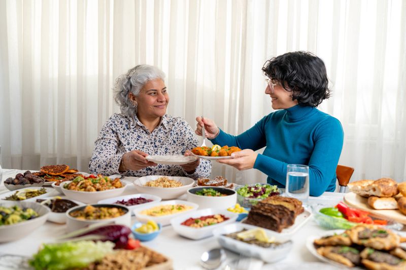 A senior woman and her adult daughter sitting at a full table, eating and chatting. Representing modern Turkish family life and daily social routines.