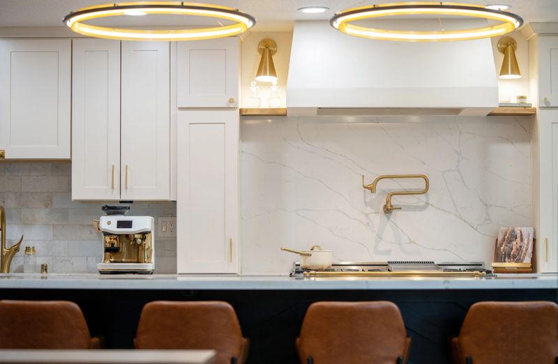Bright modern kitchen interior with cream cabinetry, marble backsplash, gas range and brass fixtures in a clean contemporary home.