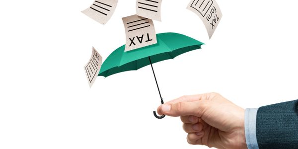 Hand holding umbrella protecting from falling tax documents.