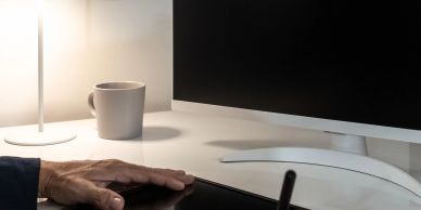 Hand using a stylus tablet near a monitor and coffee cup.