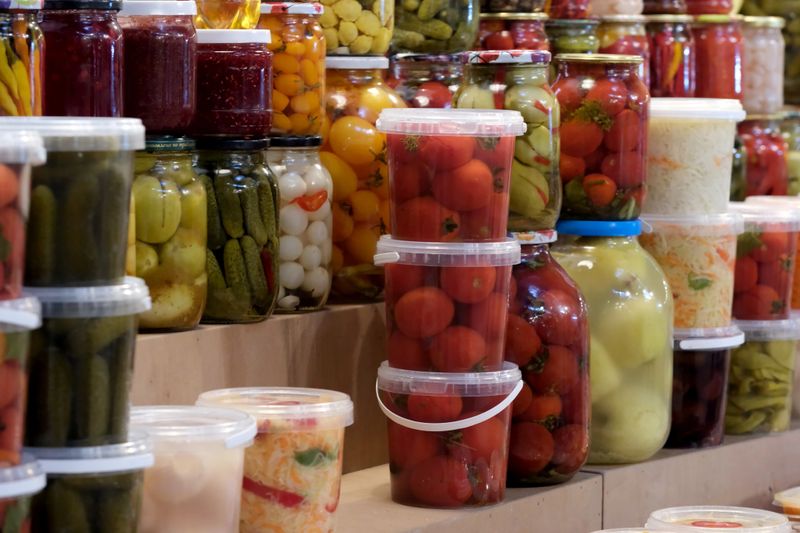 Bright jars filled with pickled vegetables are stacked in a bustling market scene. Kyiv, Ukraine. December 12, 2025.