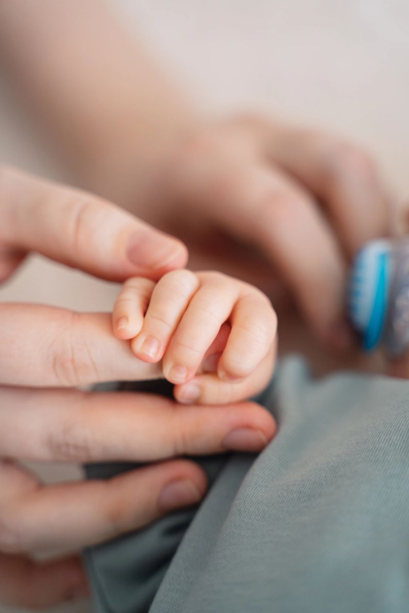 Soft close up of tiny newborn baby hand gently holding parent finger. Intimate family moment, love, bonding, trust and parenthood concept in natural light.