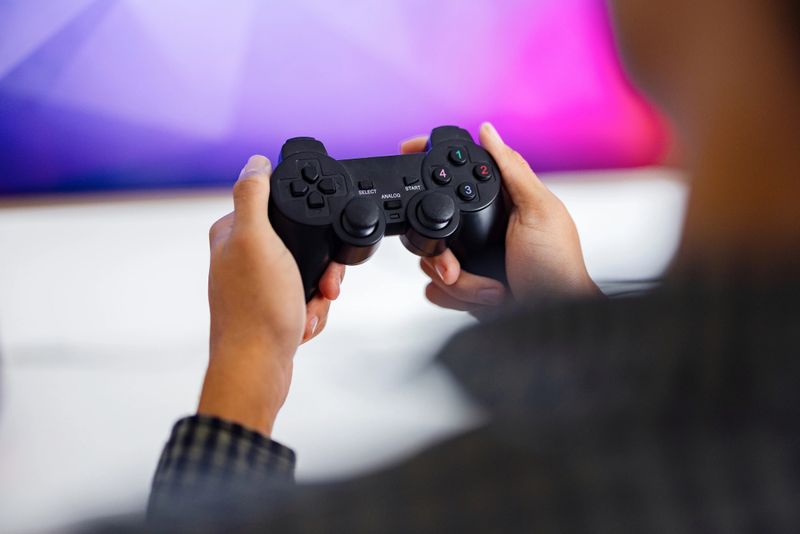 Person holding a black game controller and playing on a TV with a colorful blurred background.