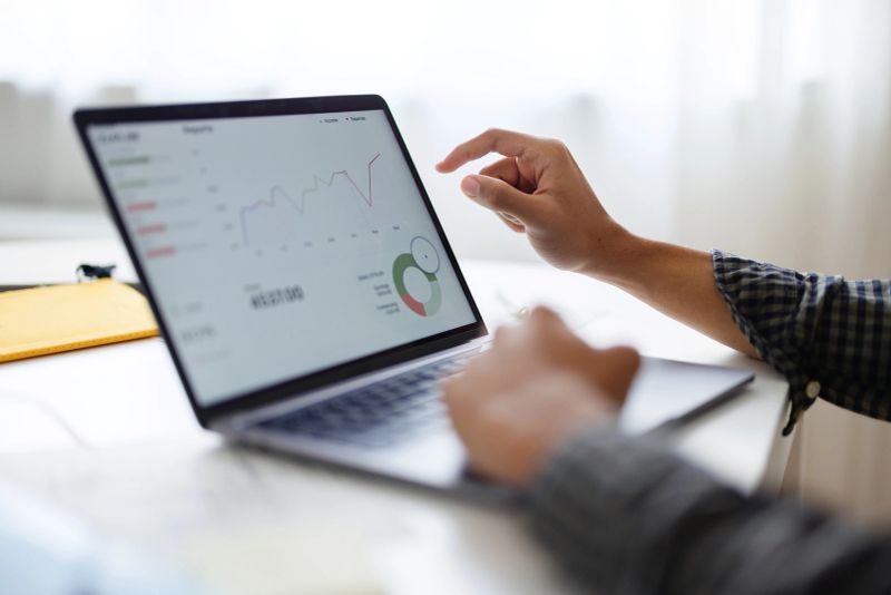 Person gestures at business analytics and charts on a laptop screen in a bright modern office.