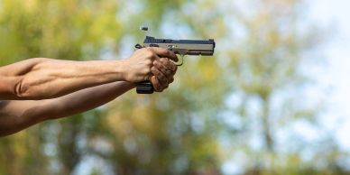 Hands aiming a handgun outdoors.