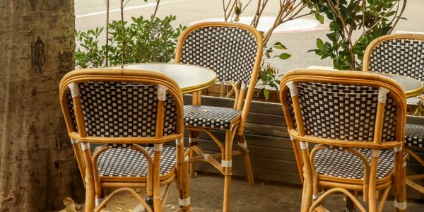 Outdoor cafe seating with woven rattan chairs and round tables.