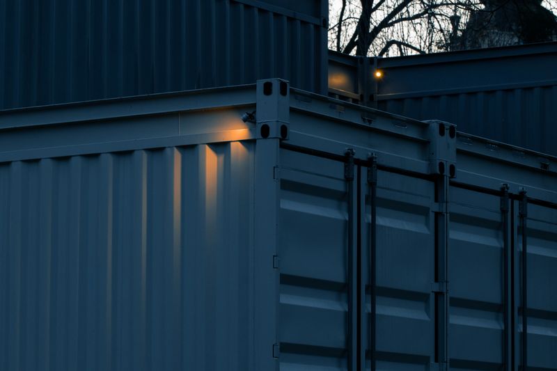 Close-up view of industrial shipping containers stacked outdoors during twilight, highlighting the textured metal and subtle illumination