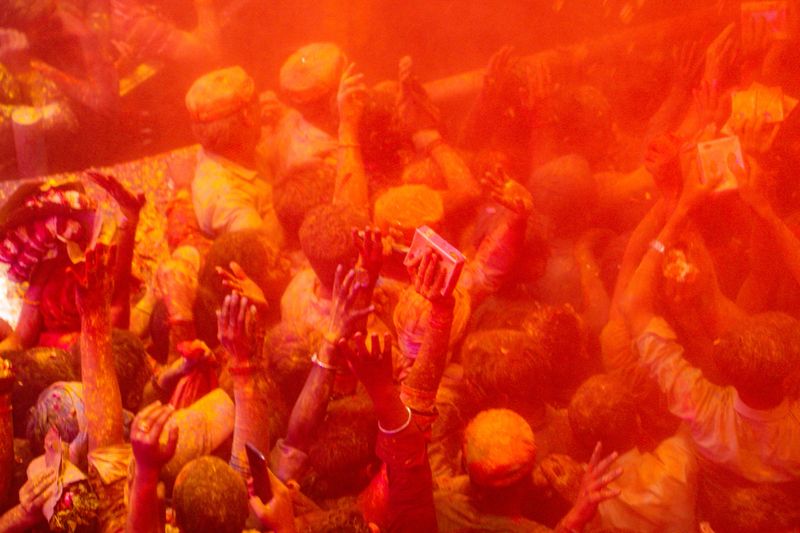 Close view of a tightly packed crowd covered in orange colored powder (gulal) during Holi festival in Vrindavan, Mathura, Uttar Pradesh. Expressive faces and raised hands reflect communal celebration.
