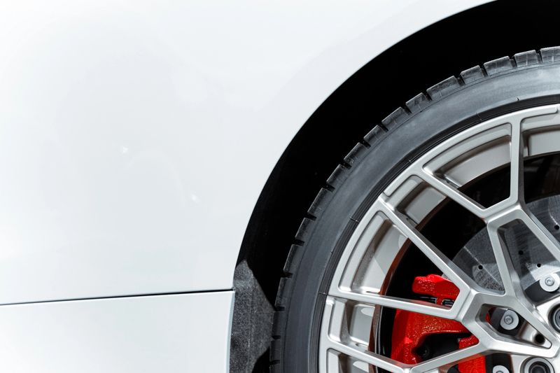 Detailed view of a modern automobile wheel featuring a polished alloy rim, performance tire, and vibrant red brake caliper, highlighting automotive engineering and design
