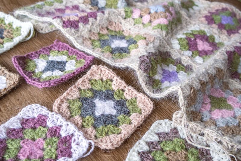 Colorful granny square crochet layout arranged as seamless textile pattern. Handmade pastel squares forming cozy vintage inspired fabric background.