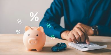 Person calculating finances with piggy bank and toy car.
