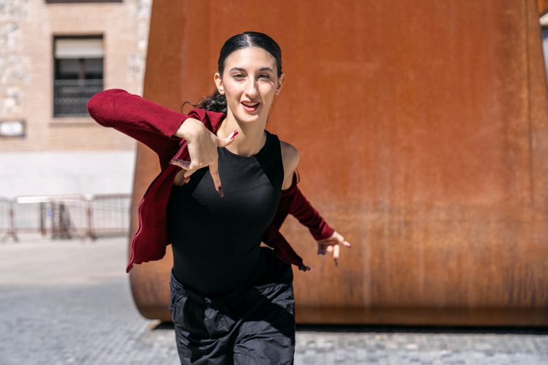 Female street dancer performing hip hop moves in an urban setting, expressing energy and personal style while looking at the camera